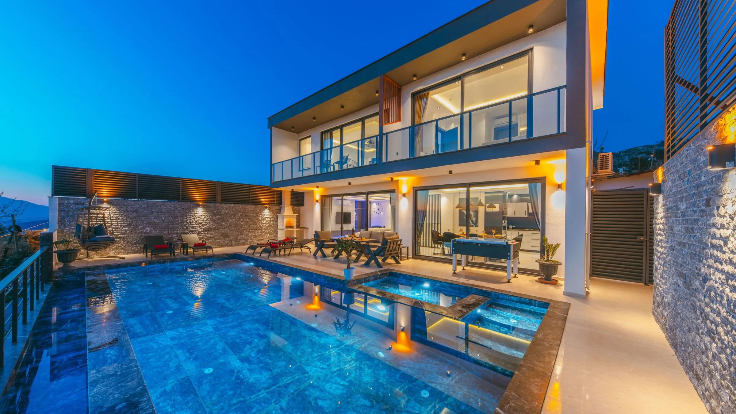 Two-storey modern villa with glass balconies and a lit pool at dusk