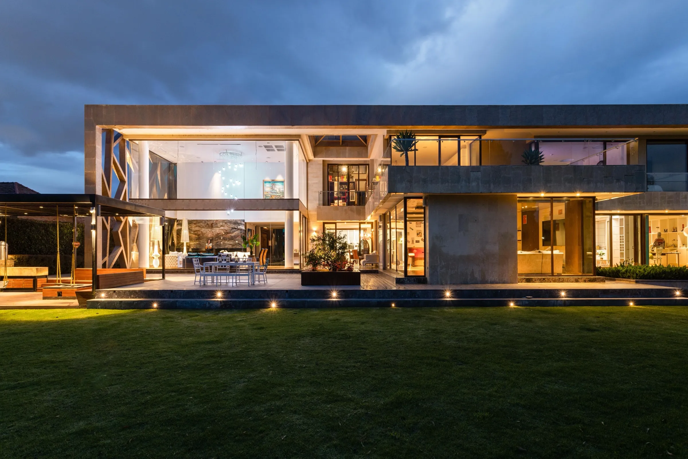 Glass villa at dusk with lit interiors and a lawn